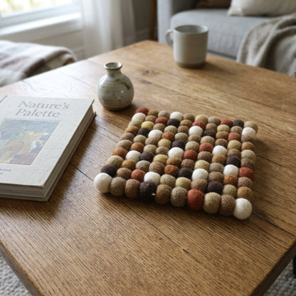 Woolen ball trivet on a wooden table with a book and small vase in a home setting