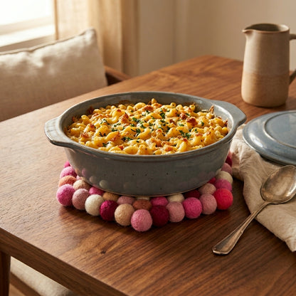 Macaroni and cheese in a gray dish on a wooden table with a colorful pom-pom trivet.