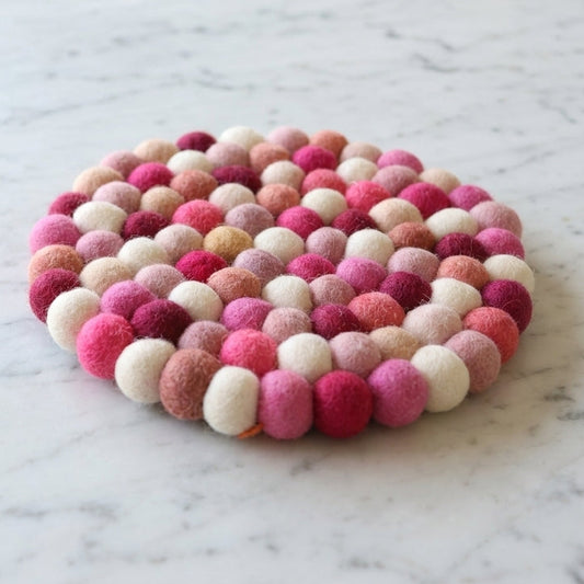 Round felt ball trivet in pink and white on a marble surface
