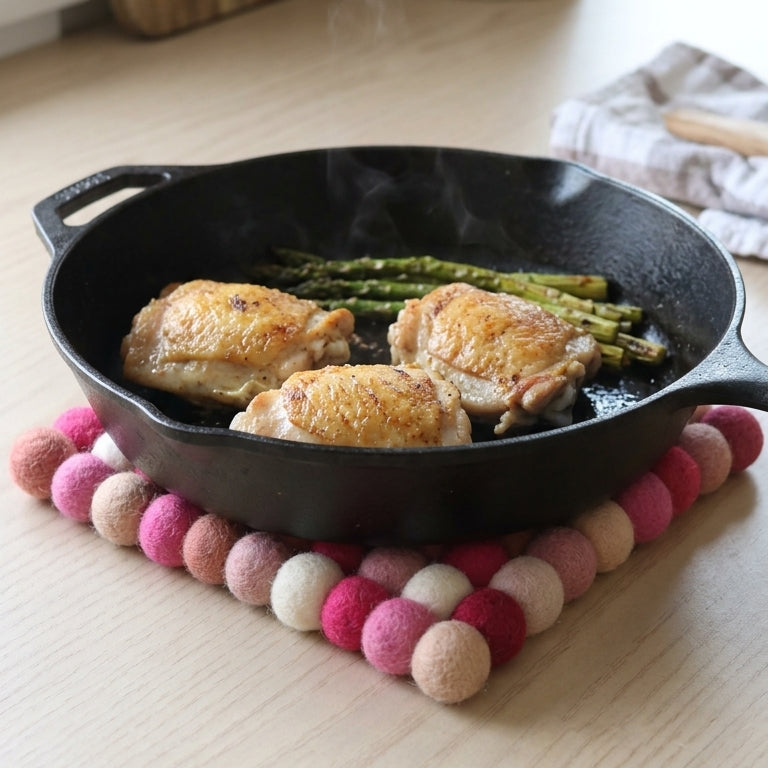 Black cast iron skillet with roasted chicken and asparagus on a wooden surface with a colorful felt trivet.