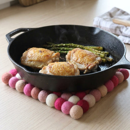Black cast iron skillet with roasted chicken and asparagus on a wooden surface with a colorful felt trivet.