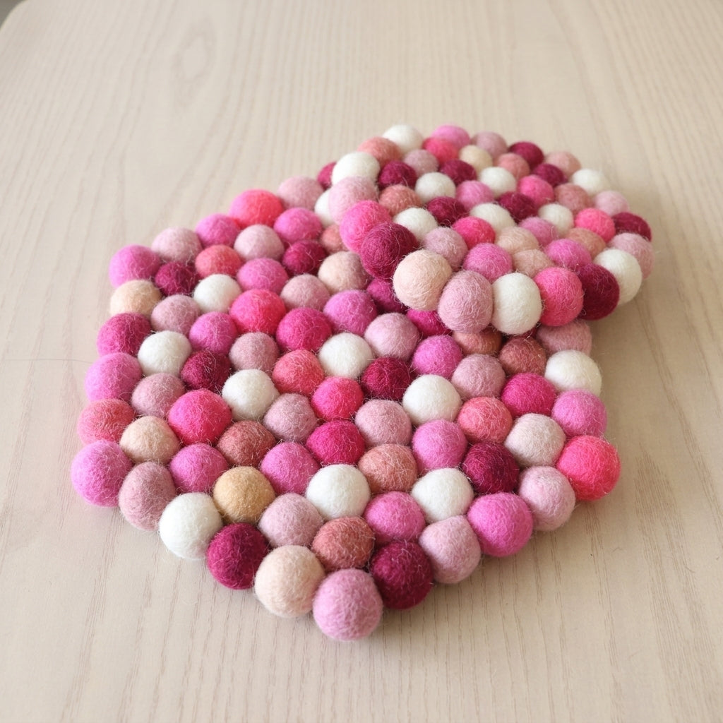 Heart-shaped felt ball coaster in pink and white on a light wooden surface