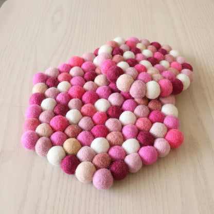 Heart-shaped felt ball coaster in pink and white on a light wooden surface