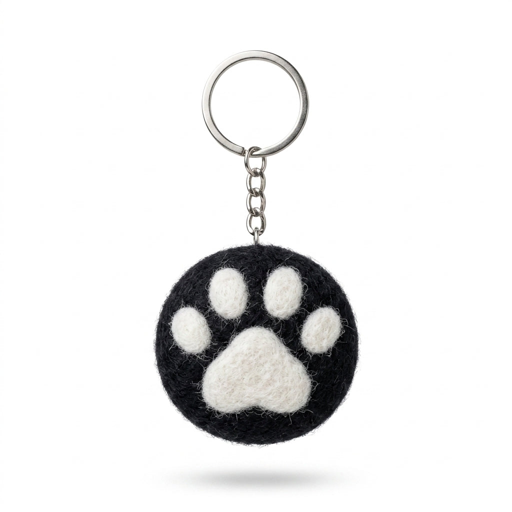 Black wool felt cat paw keyring with white paw print with a paw print design on a white background