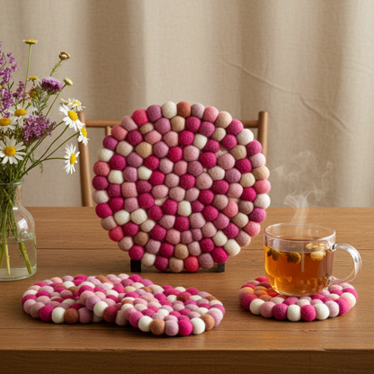 Set of colorful felt ball coasters on a wooden table with a cup of tea and flowers.