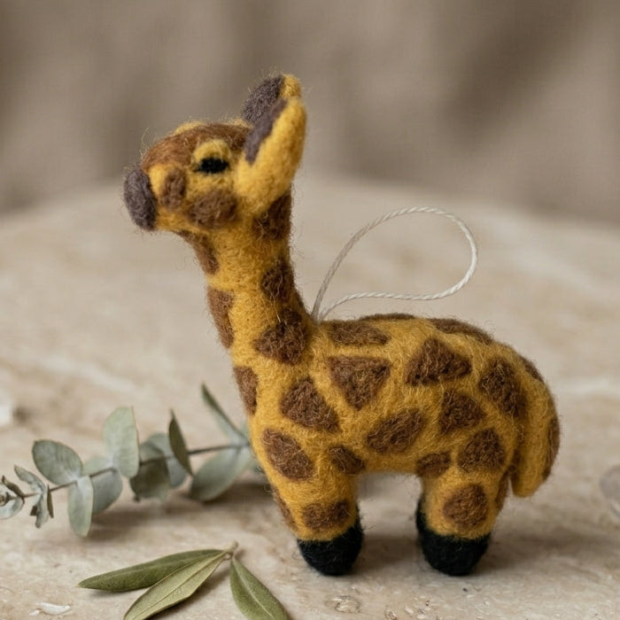 Handmade wool felt giraffe ornament on textured surface with green leaves
