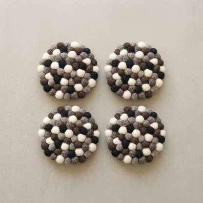 Four round Monochrome Pebble Black wool felt coasters handmade in Nepal, neutral absorbent non-scratch drink coasters for wooden tables, minimalist homes, host gifts and new home buyers with a pattern of white, black, and gray balls on a light gray background.