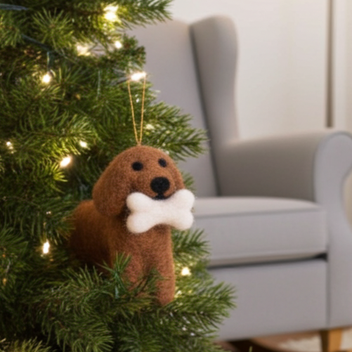 Handmade wool felt spaniel dog ornament with floppy earst with a bone on a Christmas tree in a living room setting.