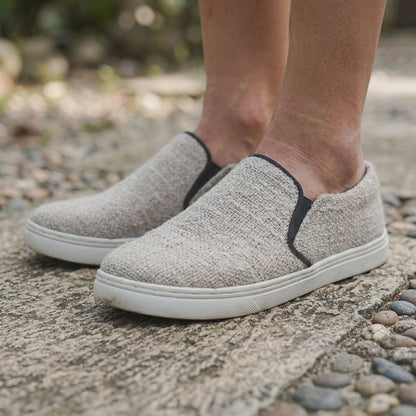 Gray PURE HEMP vegan slip-on shoes with white biodegradable rubber soles worn on a stone surface