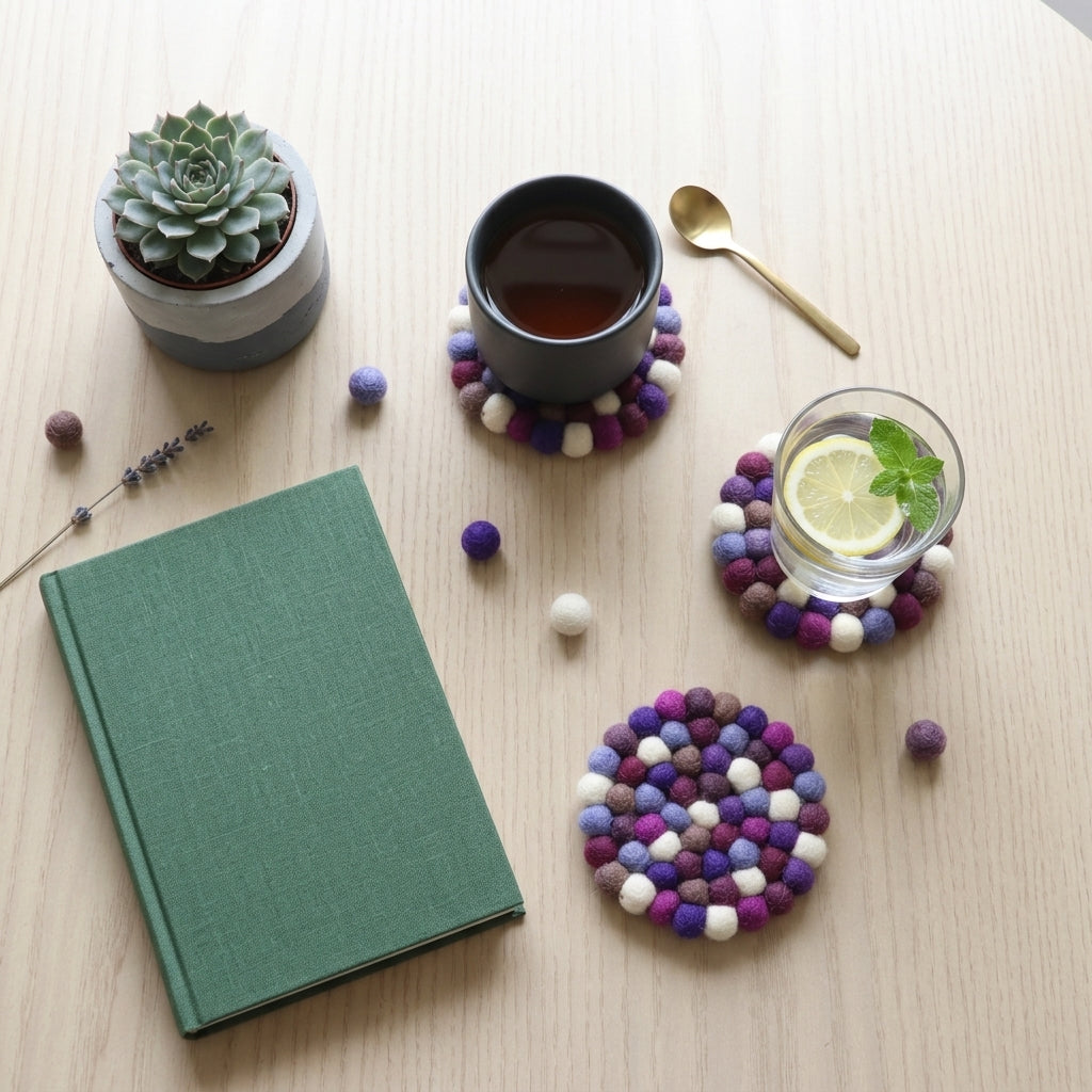 Green notebook on a wooden table with Plum Violet Purple wool felt coasters handmade in Nepal, jewel tone absorbent non-scratch drink coasters for wooden tables, tea lover gifts, host gifts and new home buyers, a cup of tea, a glass of water, and a small plant.
