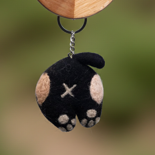Handmade wool felt cat back keyrings in assorted colours hanging from a wooden hanger with a blurred green background