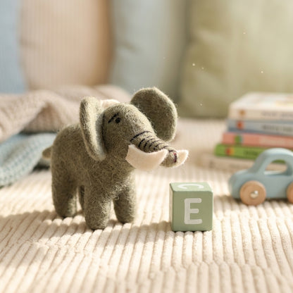 Handmade elephant felt ornament on a textured surface with a letter 'E' block and toys in the background