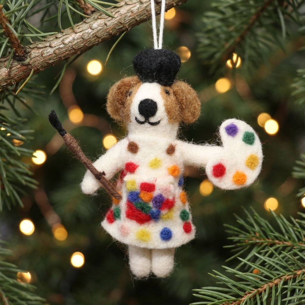 Decorative ornament of a dog in a colorful dress holding an artist's palette, hanging on a Christmas tree.