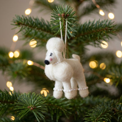Handmade wool felt poodle dog ornament t hanging on a Christmas tree with lights in the background