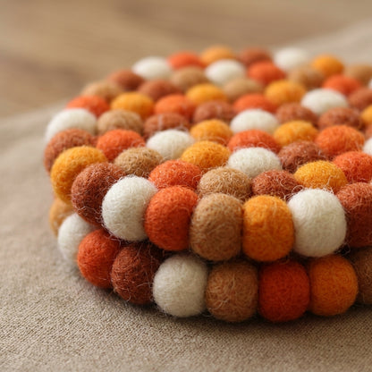 Round felt ball coaster with orange, brown, and white colors on a wooden surface