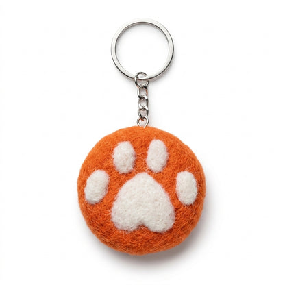 Orange wool felt cat paw keyring with white paw print on a white background