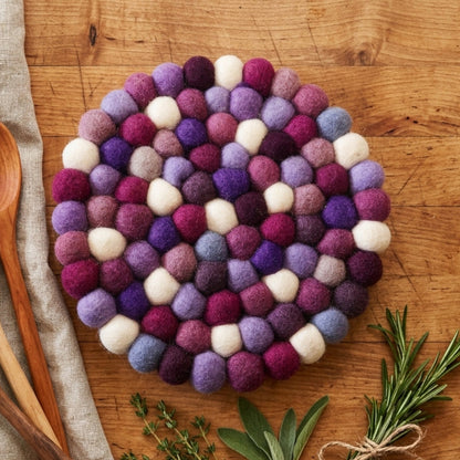 Colorful felt ball trivet on a wooden surface with wooden spoons and herbs.