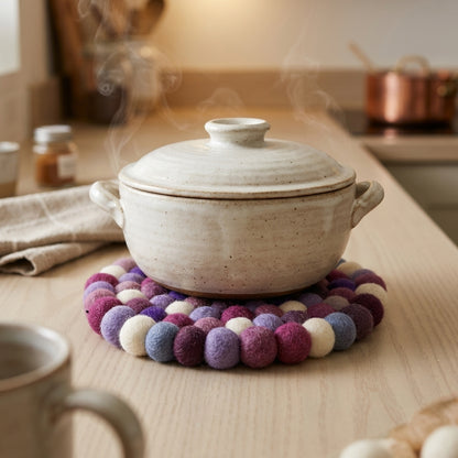 White ceramic pot on a colorful felt trivet with steam rising, placed on a wooden surface.