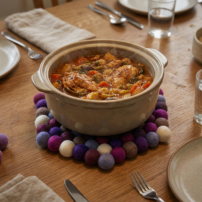 Ceramic pot with stew on a wooden table with plates, cutlery, and glasses.