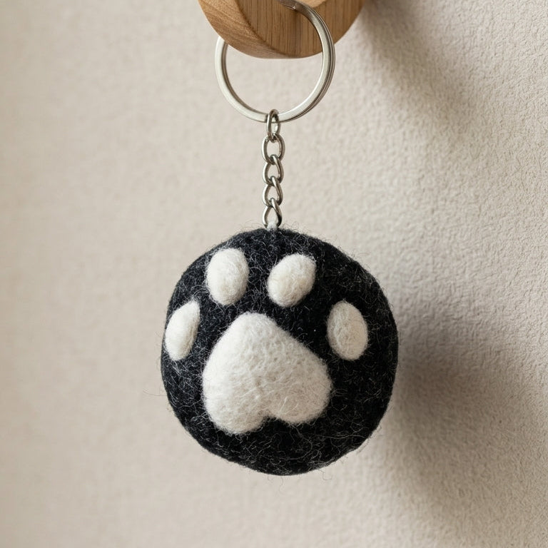 Black and white paw print keychain hanging on a wooden hook against a beige wall.