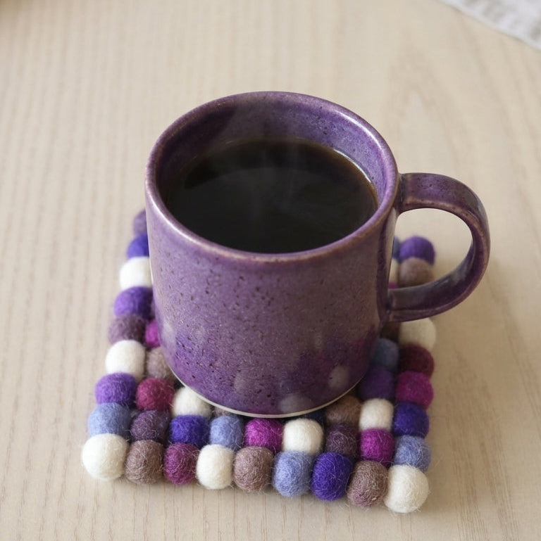 coffee mug on a Plum Violet Purple wool felt coasters handmade in Nepal, jewel tone absorbent non-scratch drink coasters for wooden tables, tea lover gifts, host gifts and new home buyerson a wooden surface