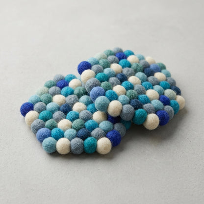 Felted ball Ocean Mix Blue wool felt coasters handmade in Nepal, coastal absorbent non-scratch drink coasters for wooden tables, coffee lover gifts, host gifts and new home buyerson a light gray background