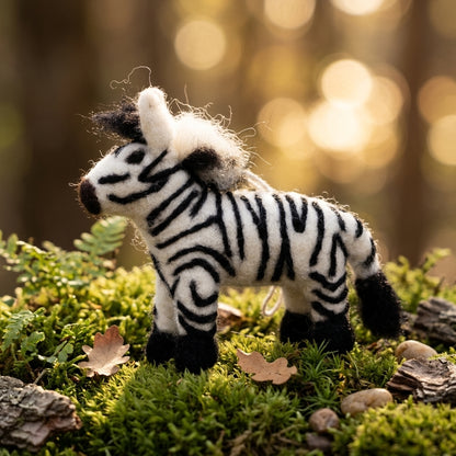 Handmade wool felt zebra ornament standing on a grassy area with a blurred forest background