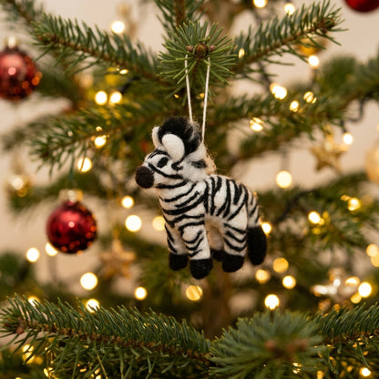 Zebra ornament hanging on a decorated Christmas tree with lights and red ornaments.