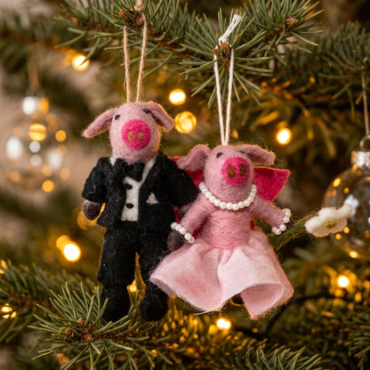 Wool felt pig bride and groom ornament one in a tuxedo and the other in a dress, hanging on a Christmas tree.
