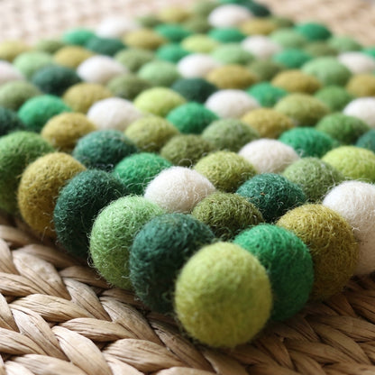 Green and white felt ball rug on a woven surface
