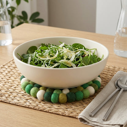 White bowl of salad on a decorative green and white trivet on a wooden table.