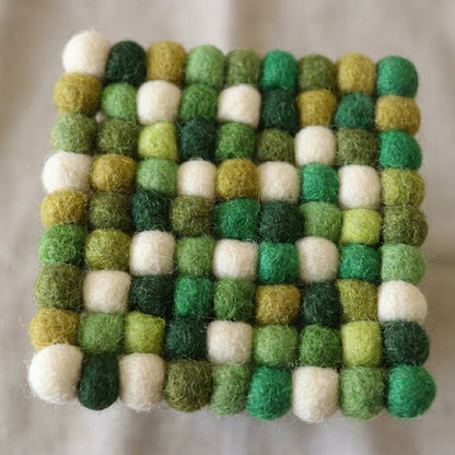 Square Forest Mix Green wool felt coasters handmade in Nepal, botanical absorbent non-scratch drink coasters for wooden tables, plant lover gifts, host gifts and new home buyers felt ball pattern on a plain background