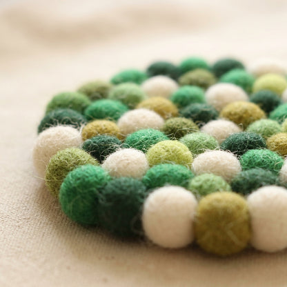 Close-up of a fForest Mix Green wool felt coasters handmade in Nepal, botanical absorbent non-scratch drink coasters for wooden tables, plant lover gifts, host gifts and new home buyers with green and white colors on a beige surface