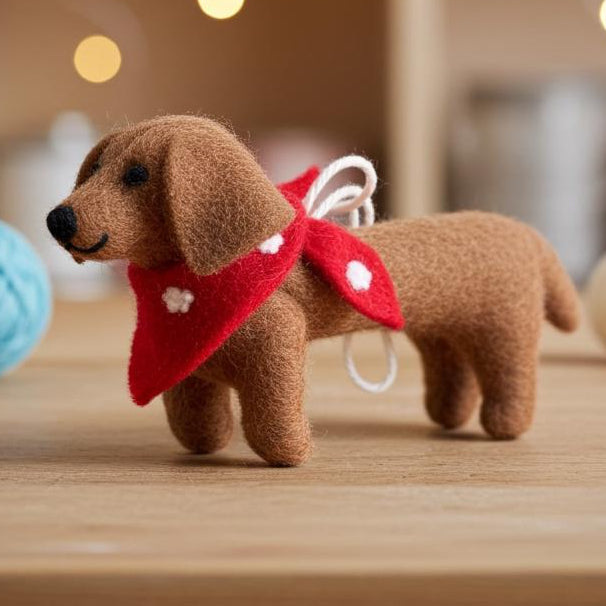 Handmade wool felt dachshund dog ornament  with a red scarf on a wooden surface with blurred lights in the background