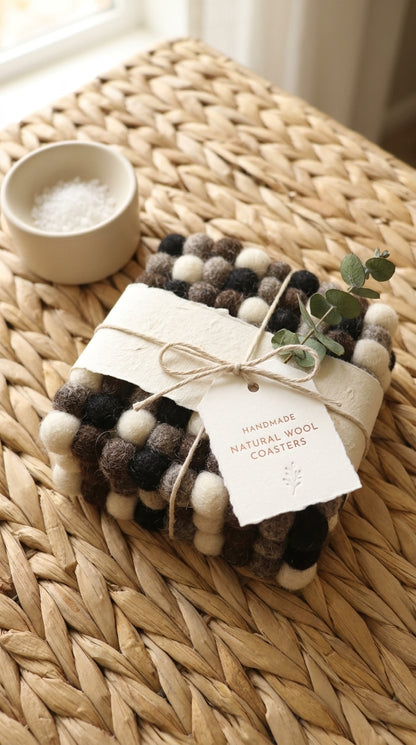 Set ofMonochrome Pebble Black wool felt coasters handmade in Nepal, neutral absorbent non-scratch drink coasters for wooden tables, minimalist homes, host gifts and new home buyerswith a tag on a woven surface