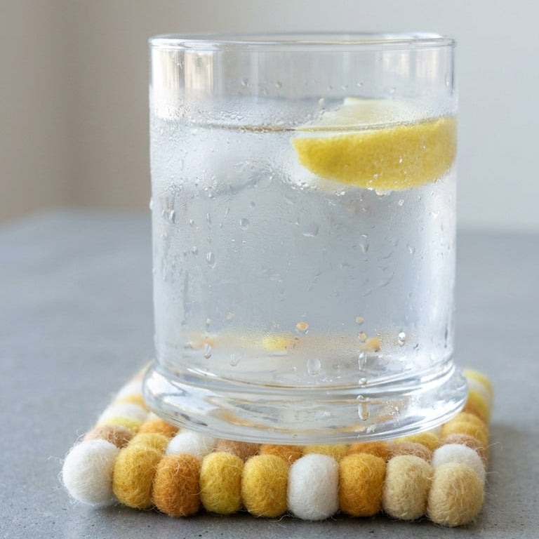 Glass of water with lemon on aMustard Yellow wool felt coasters handmade in Nepal, warm absorbent non-scratch drink coasters for wooden tables, teacher gifts, host gifts and new home buyers coaster