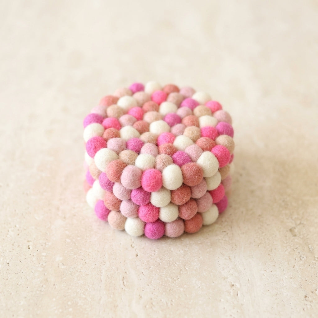 Cube-shaped object made of pink and white felt balls on a beige background