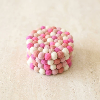 Cube-shaped object made of pink and white felt balls on a beige background
