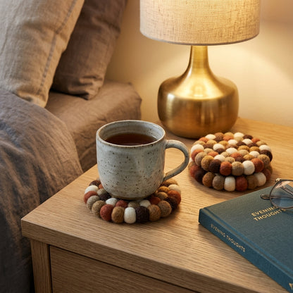 Cup of tea on a coaster with a lamp and book on a wooden surface