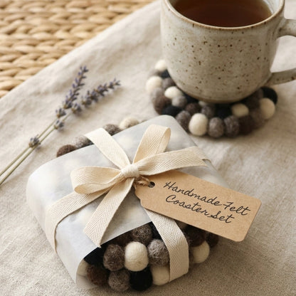 Set of handmadeMonochrome Pebble Black wool felt coasters handmade in Nepal, neutral absorbent non-scratch drink coasters for wooden tables, minimalist homes, host gifts and new home buyers with a mug of tea on a wooden table.