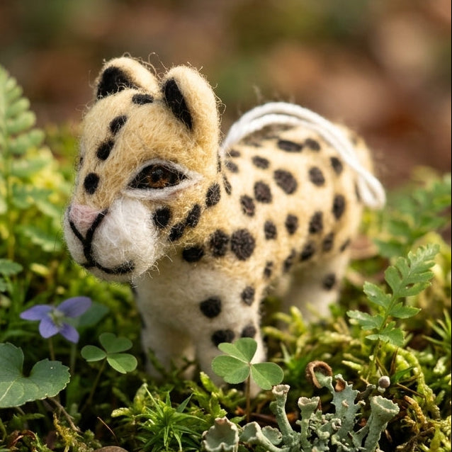 Leopard safari animal ornament made from wool felt standing on a bed of green moss and small plants.